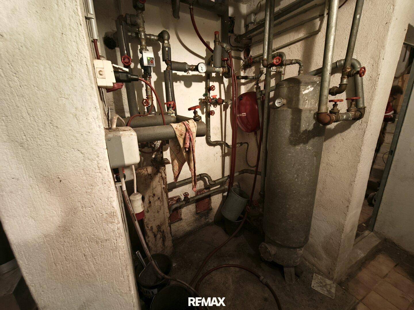 Technikraum mit komplexen Rohrleitungen, Ventilen und einem Warmwasserspeicher, typisch für die Haustechnik.