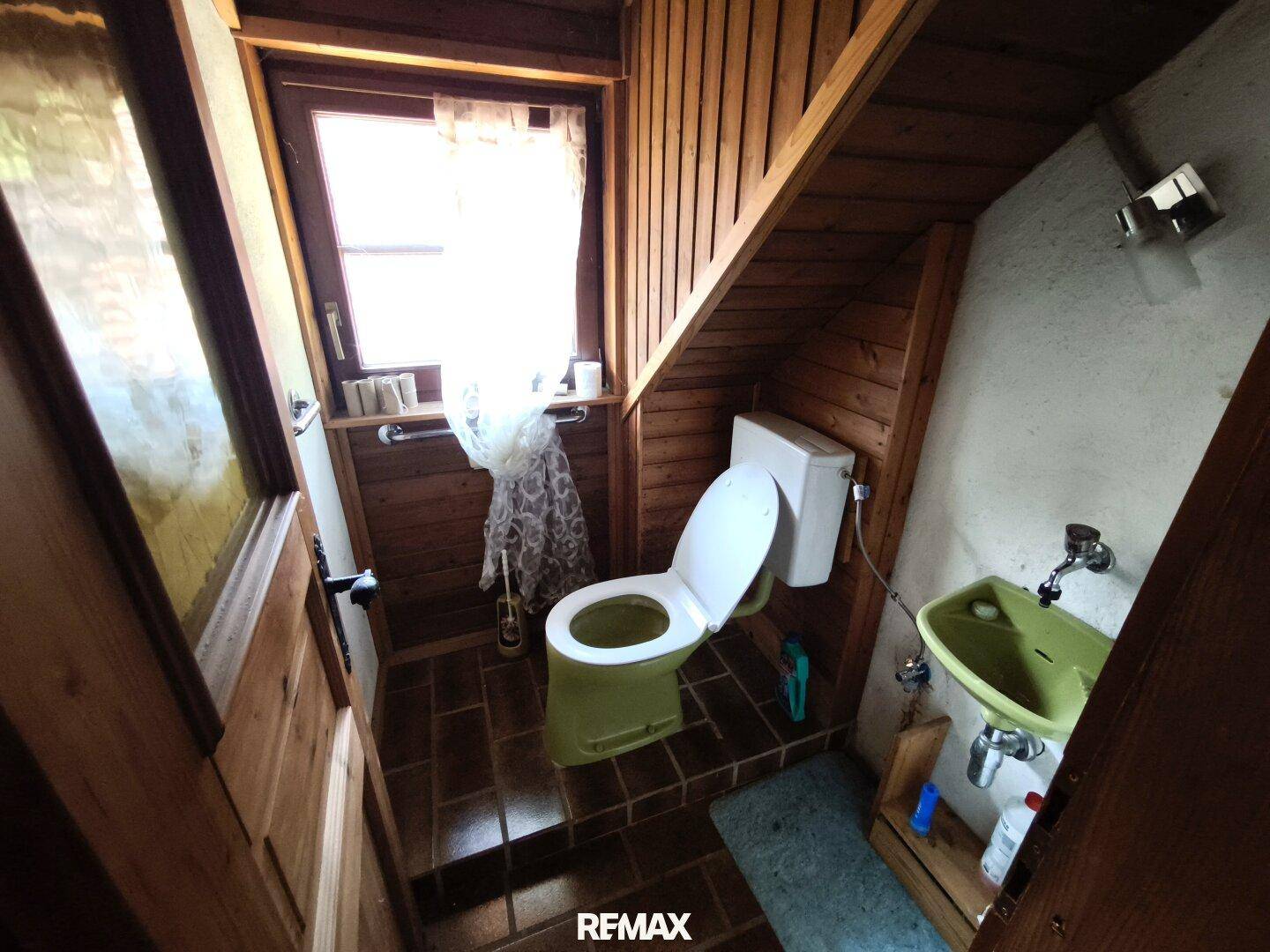 Kleines WC mit Fenster, Holzverkleidung und einfacher Ausstattung.