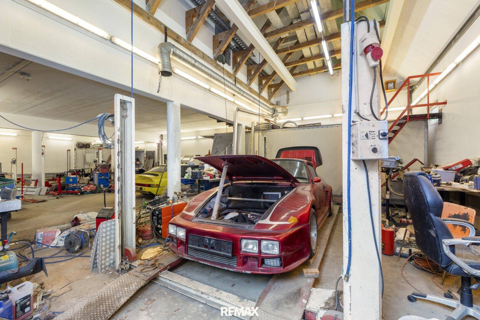 Große Werkstatt mit einem Auto auf der Hebebühne und sichtbarer Holzkonstruktion des Daches.