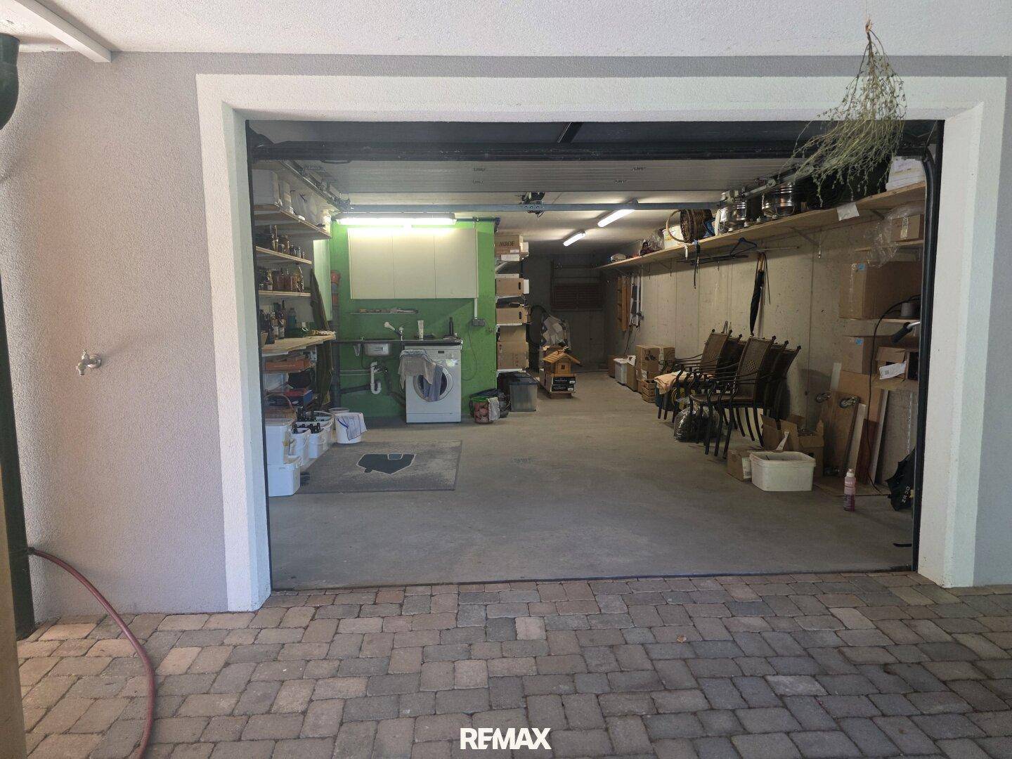 Geräumige Garage, die auch als Hauswirtschaftsraum mit Waschmaschine und Regalen dient.