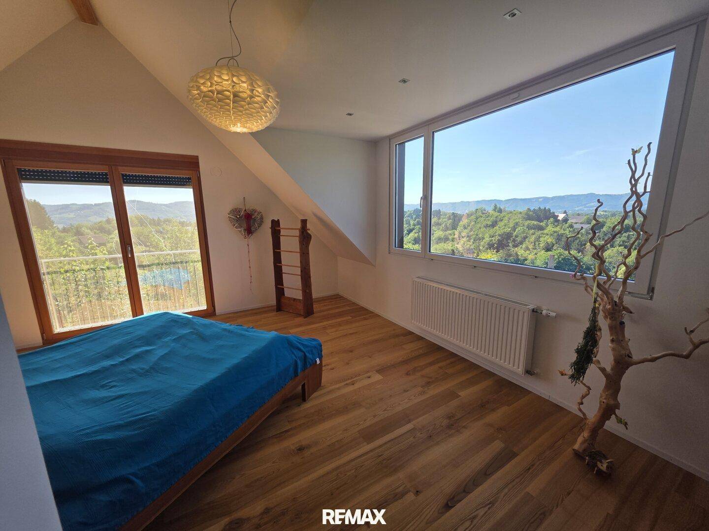 Helles Schlafzimmer im Dachgeschoss mit Holzboden, großen Fenstern und weitem Blick ins Grüne.