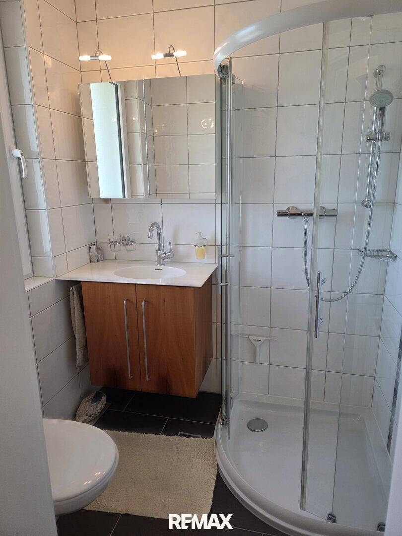 Kleines Badezimmer mit Duschkabine, Waschbeckenunterschrank und weißen Fliesen.