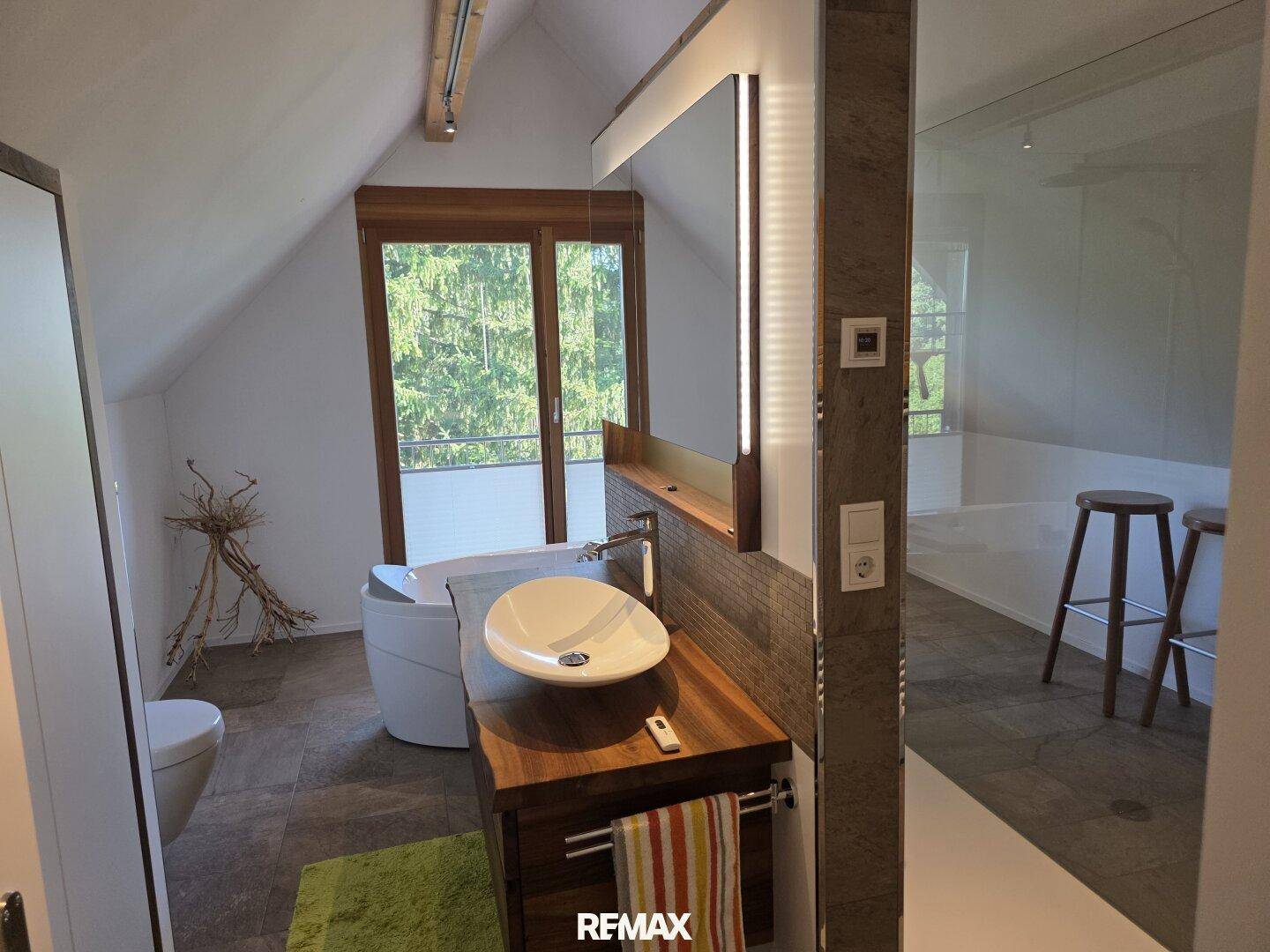 Geräumiges Badezimmer im Dachgeschoss mit Waschtisch, Aufsatzwaschbecken und Fenster mit Waldblick.