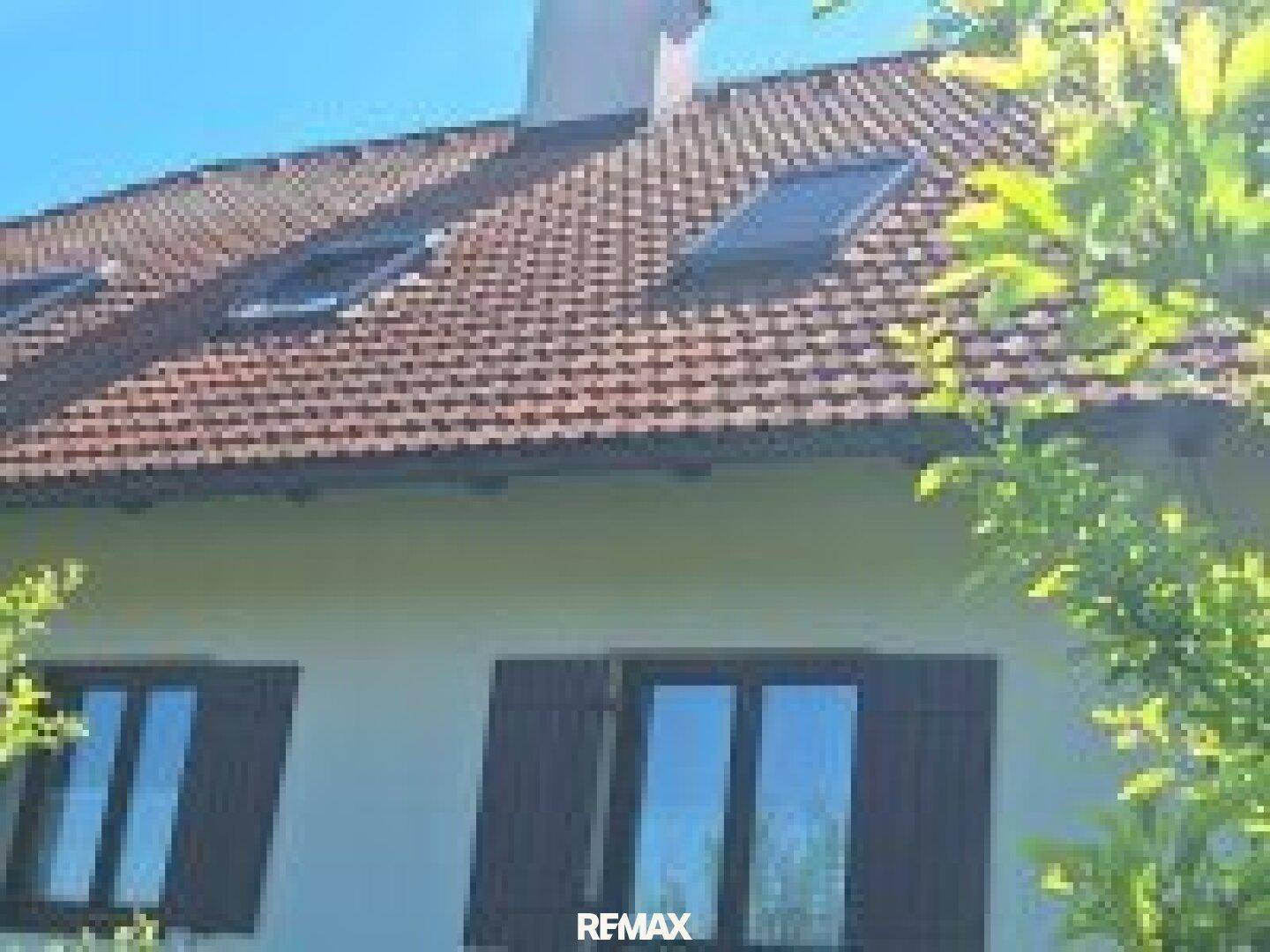 Nahaufnahme des Daches mit Ziegeln und Dachfenstern, umgeben von grünen Baumwipfeln.