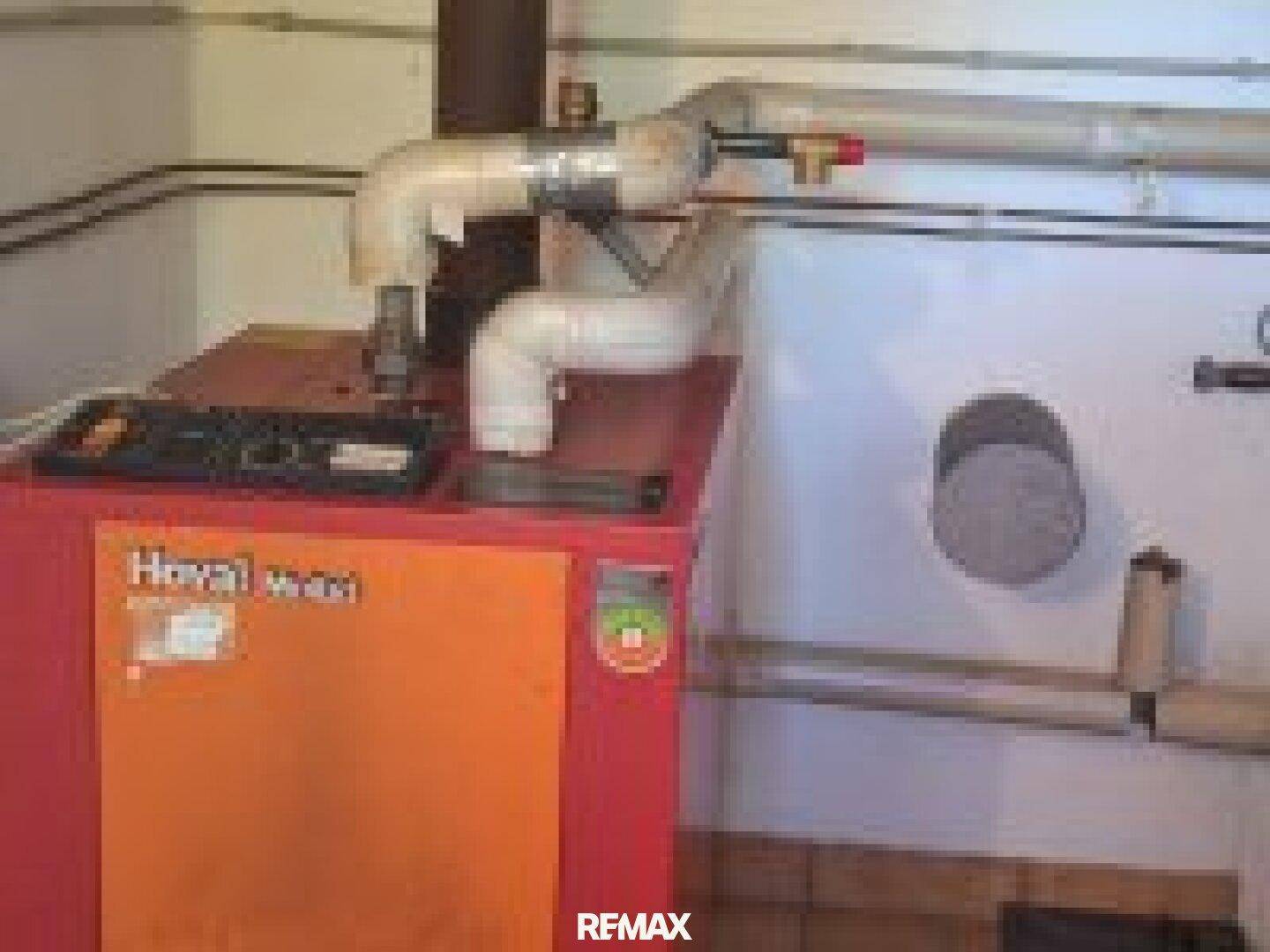 Heizungsraum mit einem orangefarbenen Heizkessel und sichtbaren Rohrleitungen für die Warmwasserversorgung.