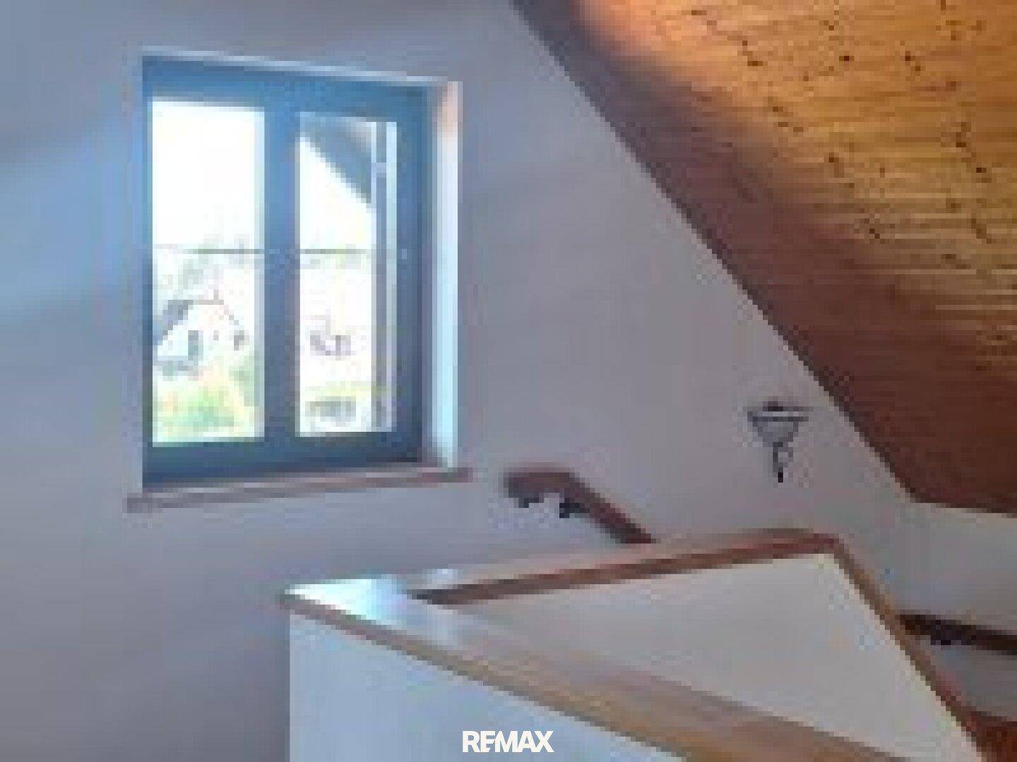 Heller Flurbereich im Dachgeschoss mit Holzdecke, Fenster und Treppengeländer.