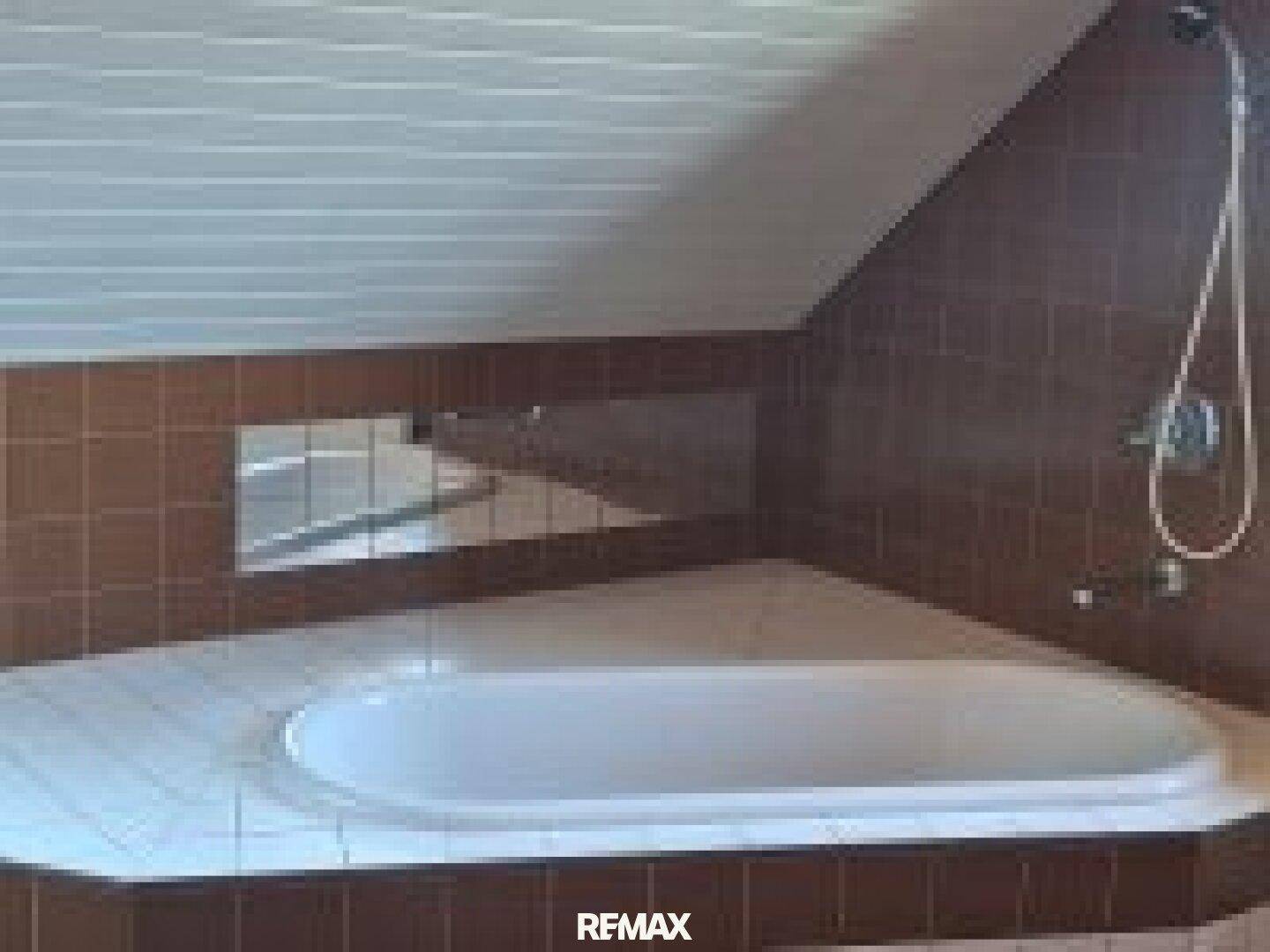 Badezimmer im Dachgeschoss mit braunen Fliesen, eingebauter Badewanne und Dachschräge.