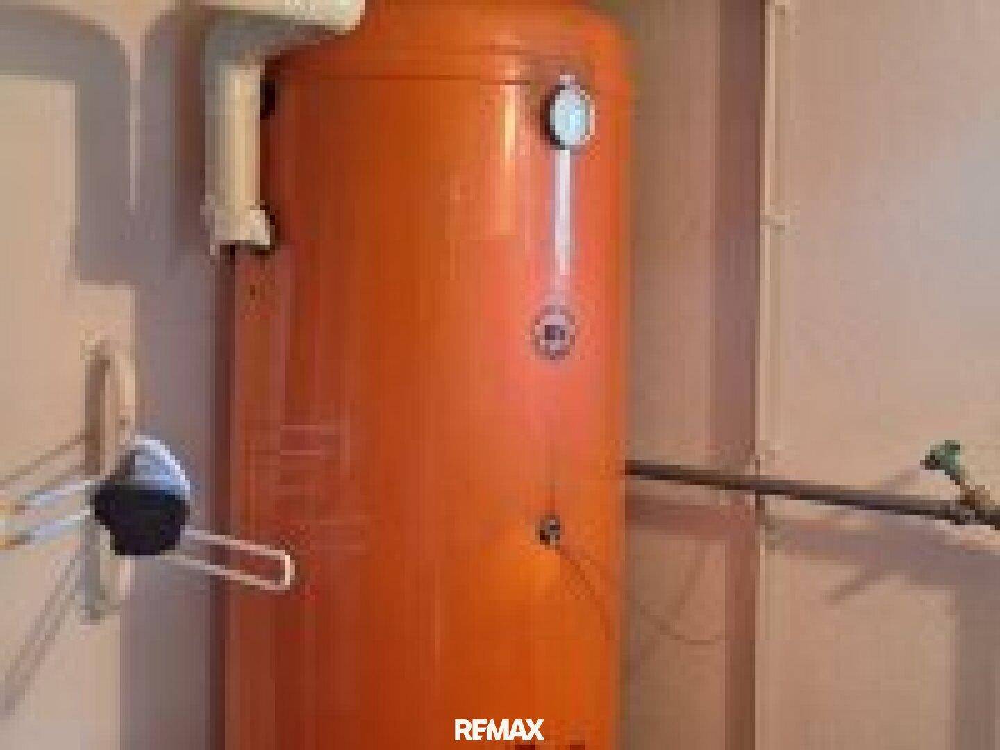 Hauswirtschaftsraum mit einem großen orangefarbenen Warmwasserspeicher und sichtbaren Installationen.