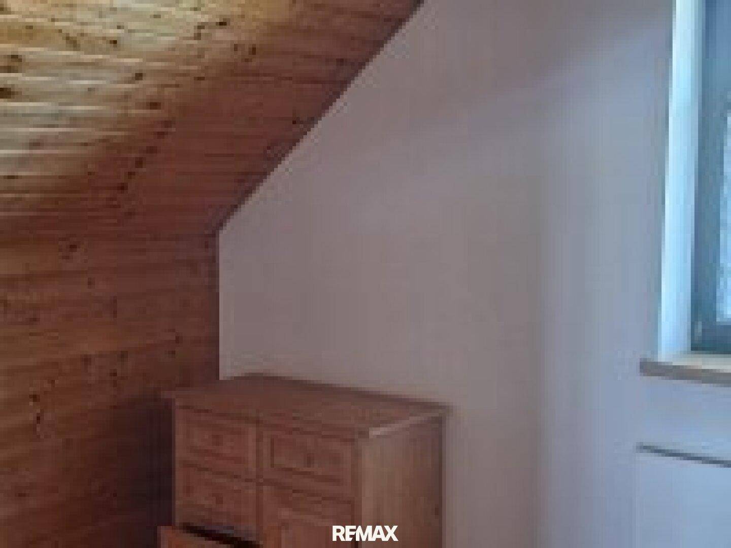 Raum im Dachgeschoss mit Holzdecke, Dachschräge und einer Kommode aus hellem Holz.