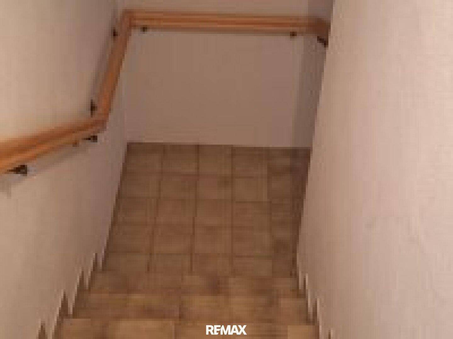 Treppenhaus mit gefliesten Stufen und Holzgeländer, das in ein Untergeschoss führt.
