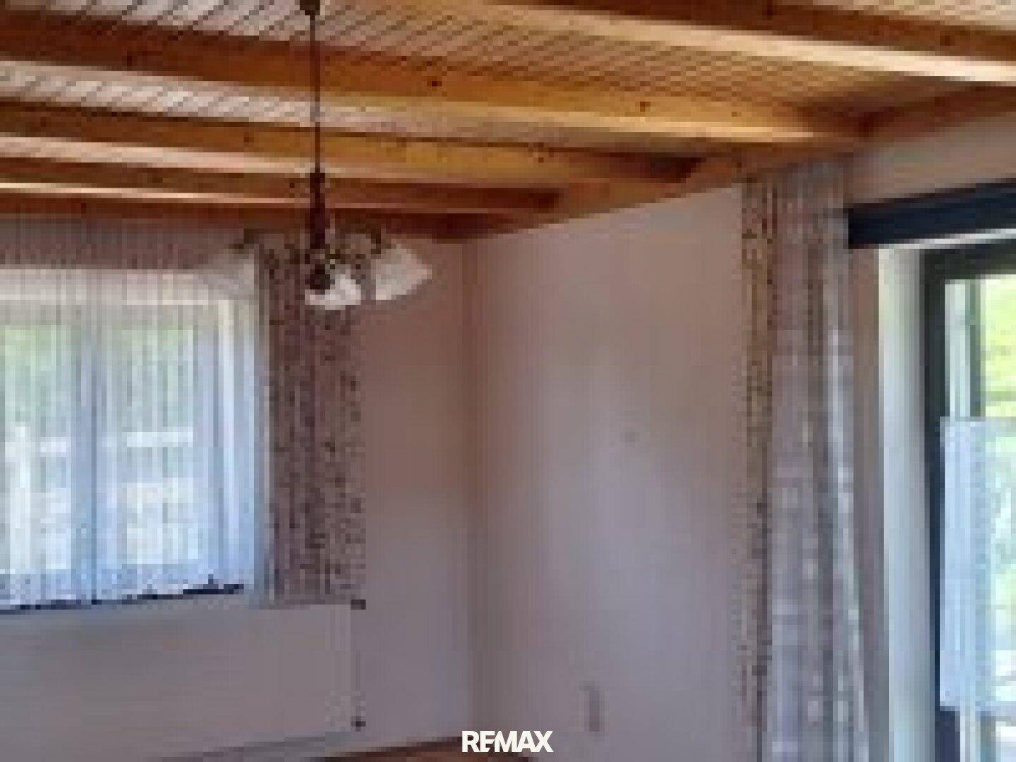 Heller Raum mit Holzdecke, großen Fenstern und Vorhängen, die viel Tageslicht hereinlassen.
