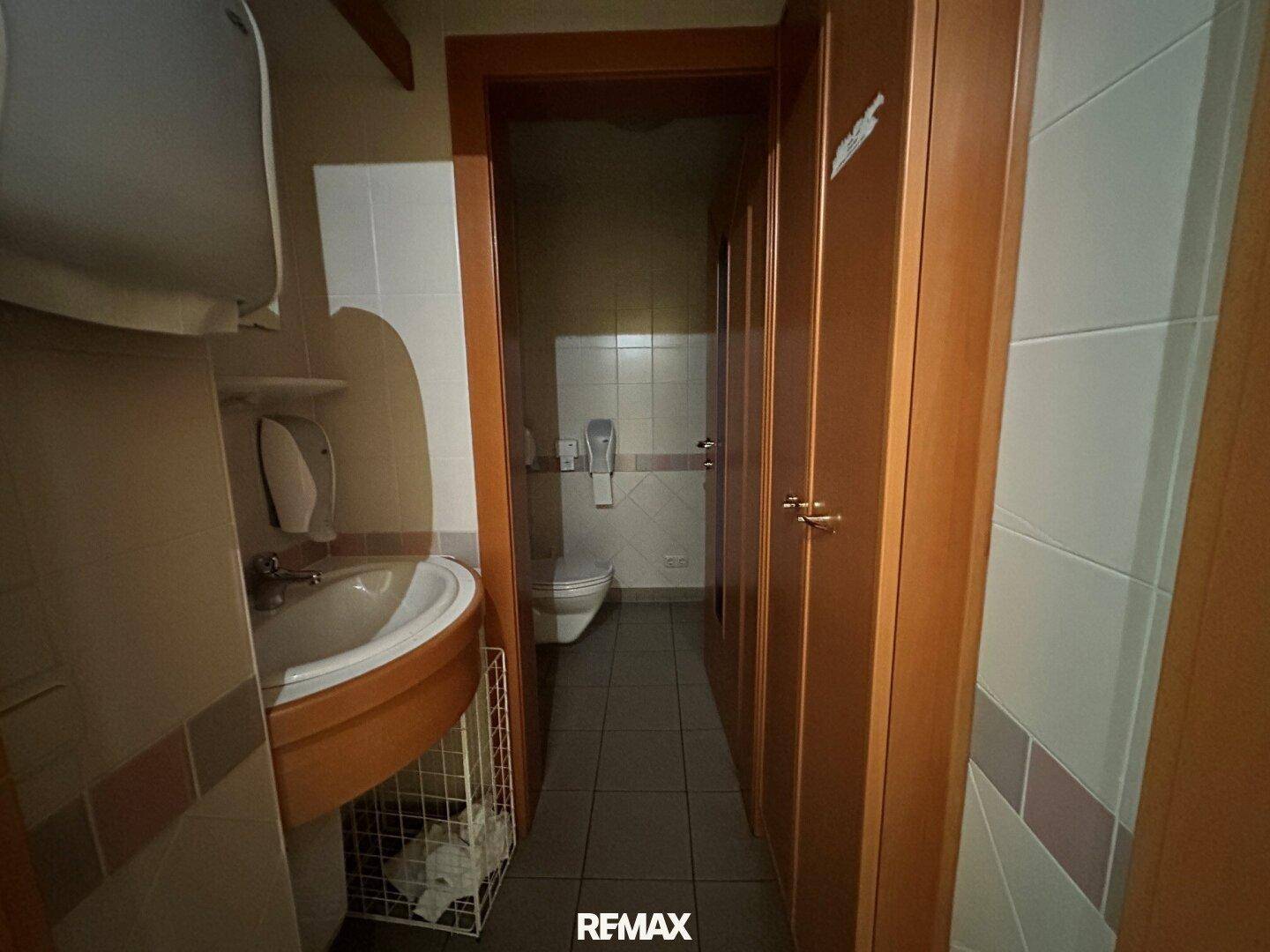 Schmaler WC-Bereich mit Waschbecken und Toilette, gefliesten Wänden und Holztüren.