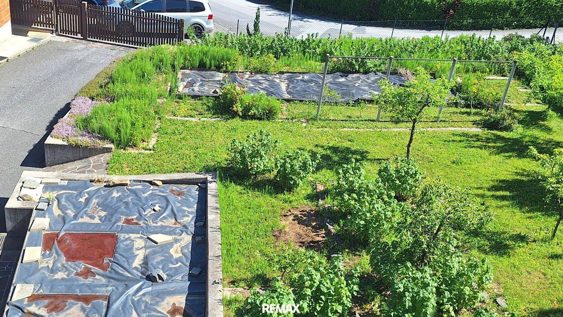 Gartenbereich mit Rasenflächen, Sträuchern und vorbereiteten Beeten neben einer Straße.