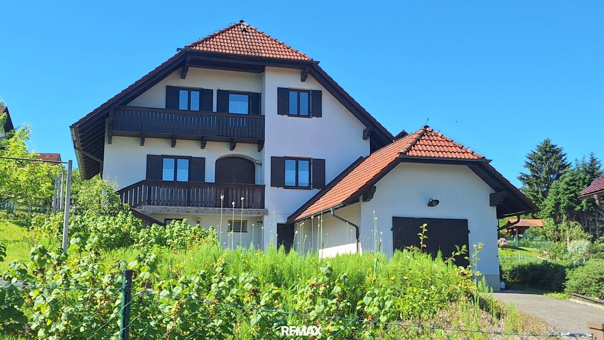 Großes Einfamilienhaus mit mehreren Balkonen und einem angrenzenden Garagengebäude.