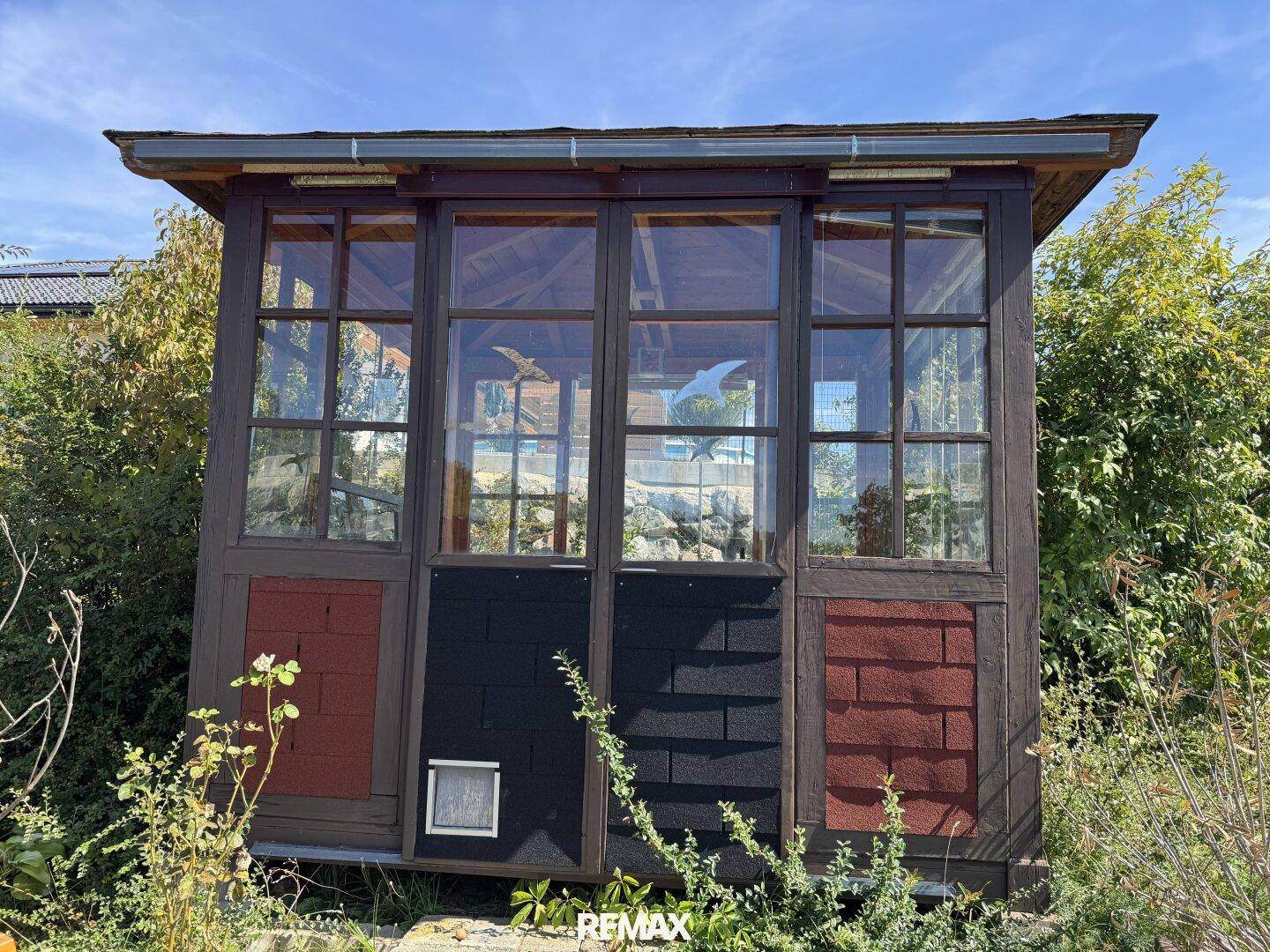 Kleines Gartenhaus mit großen Fenstern und dekorativen Elementen im Grünen.
