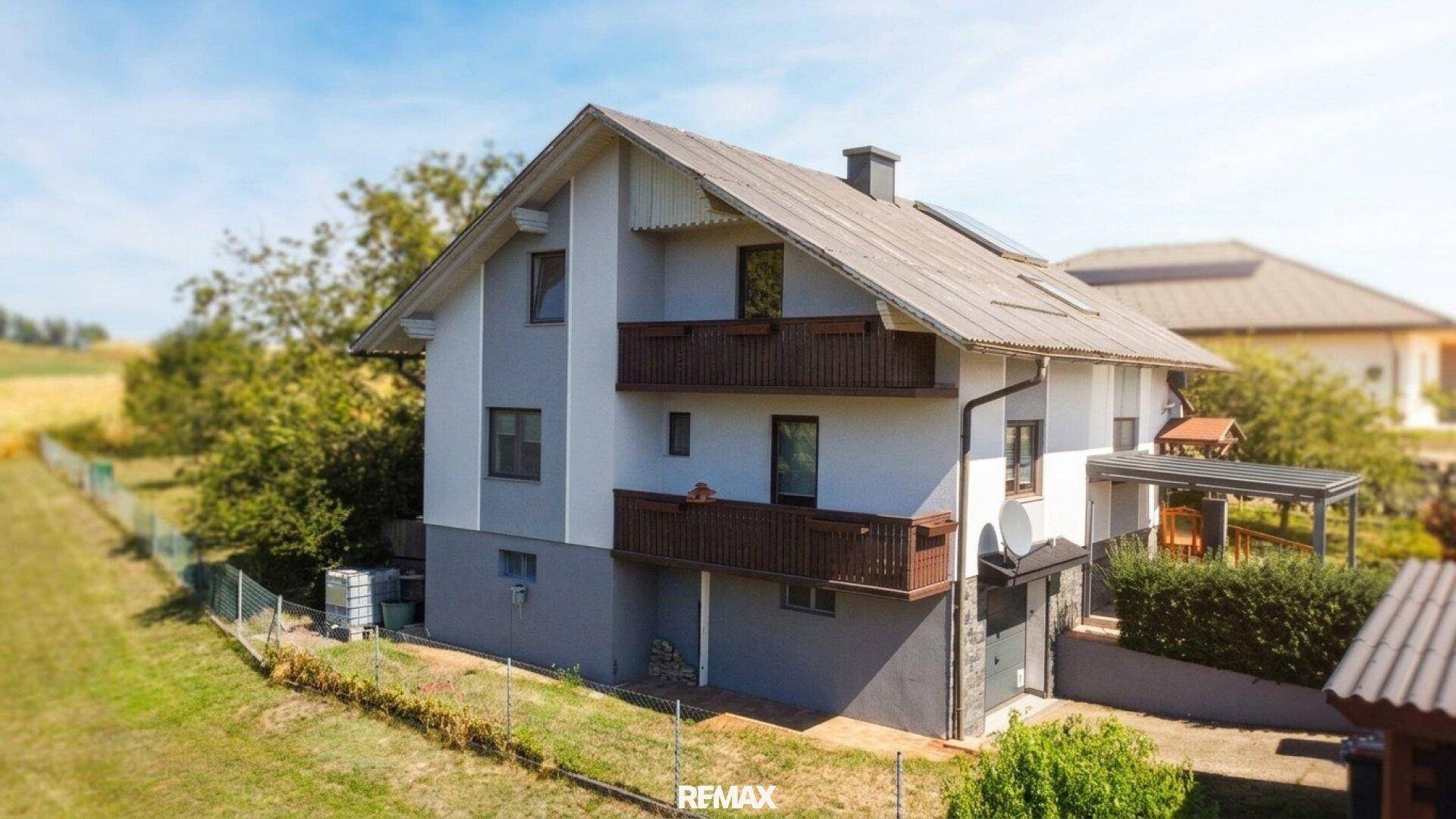 Seitenansicht des Einfamilienhauses mit mehreren Balkonen und grüner Hecke.