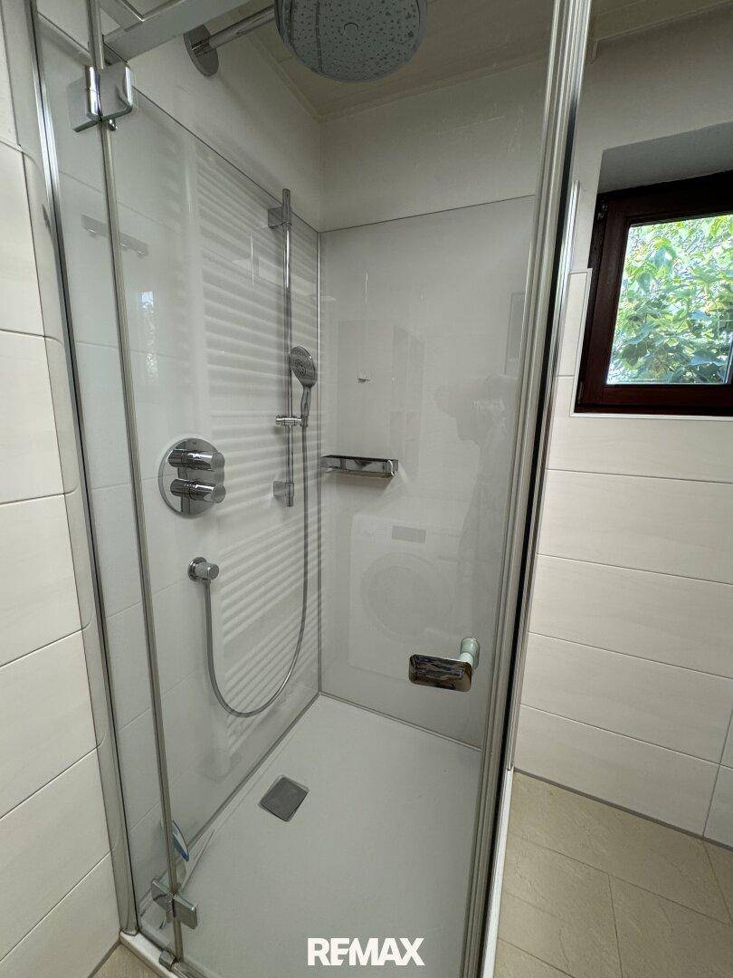 Detailansicht der modernen, ebenerdigen Dusche mit Regenduschkopf und Glasabtrennung.