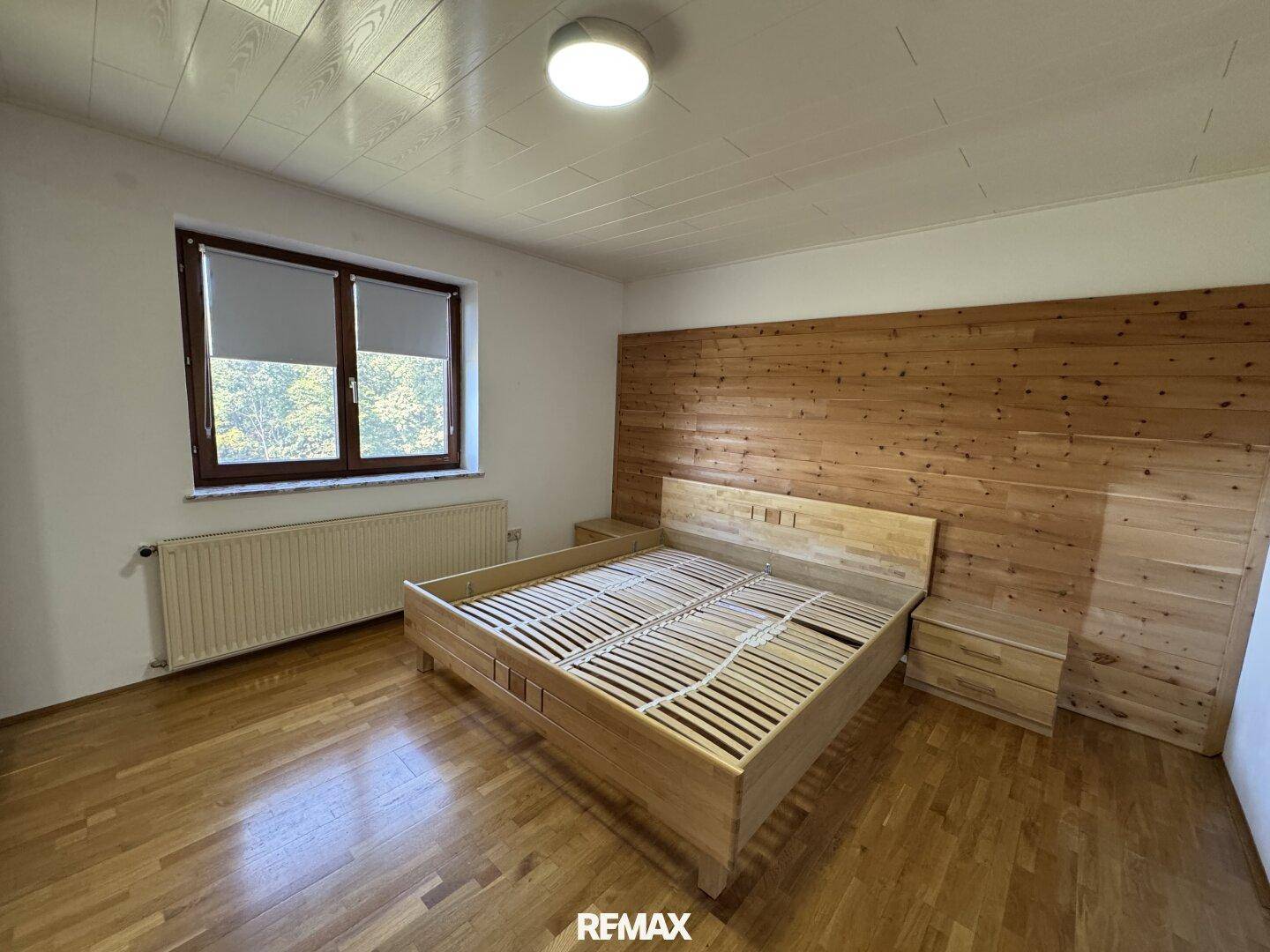 Helles Schlafzimmer mit Holzboden, Holzwandverkleidung und großem Fenster.