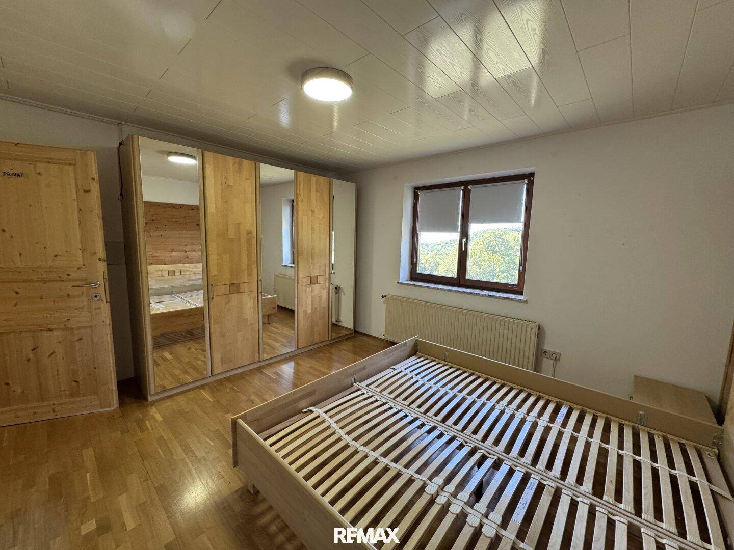 Schlafzimmer mit Holzboden, großem Spiegelschrank und Blick ins Grüne.