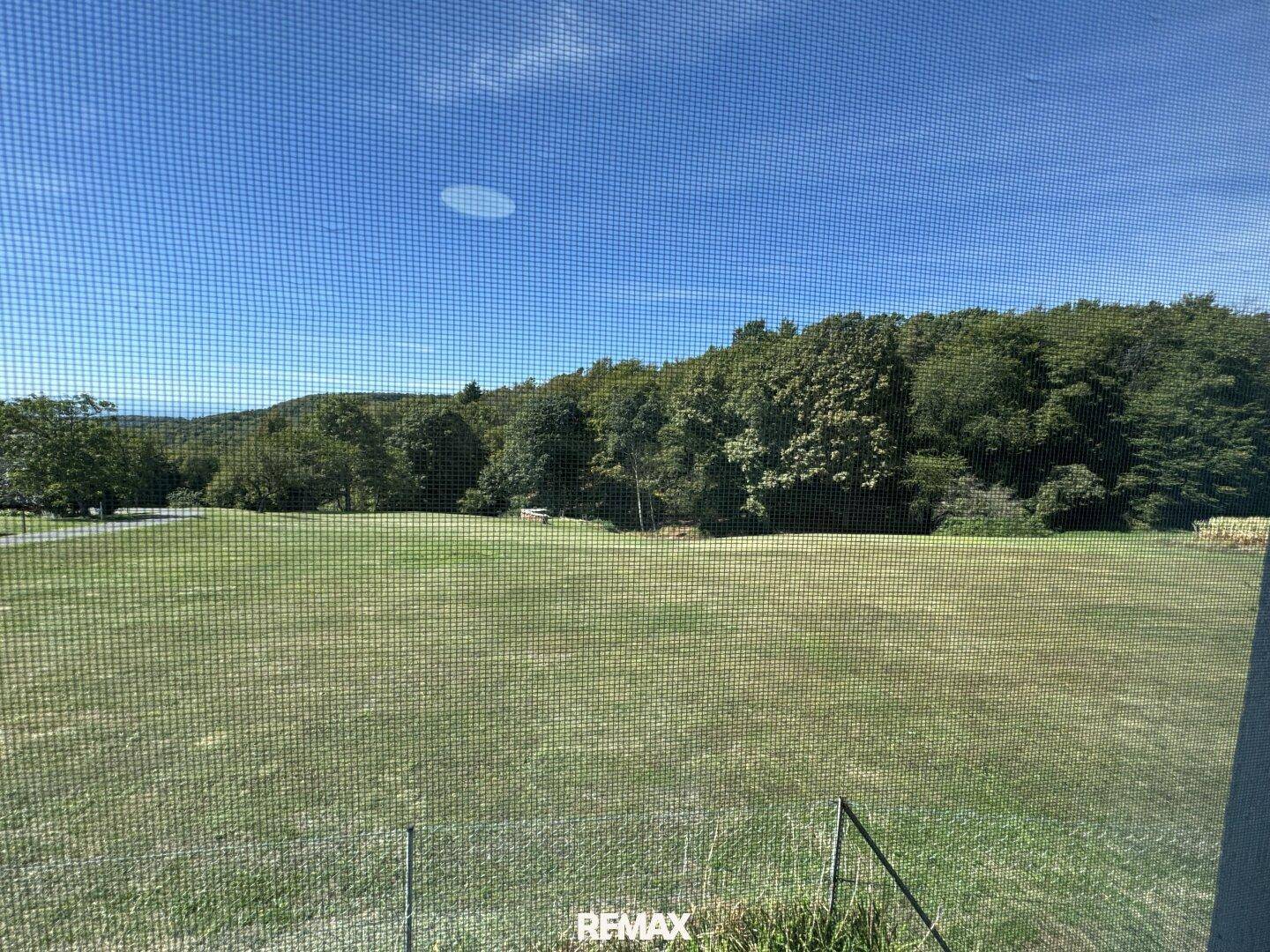 Weitläufiger Blick aus dem Fenster auf eine grüne Wiese und bewaldete Hügel.