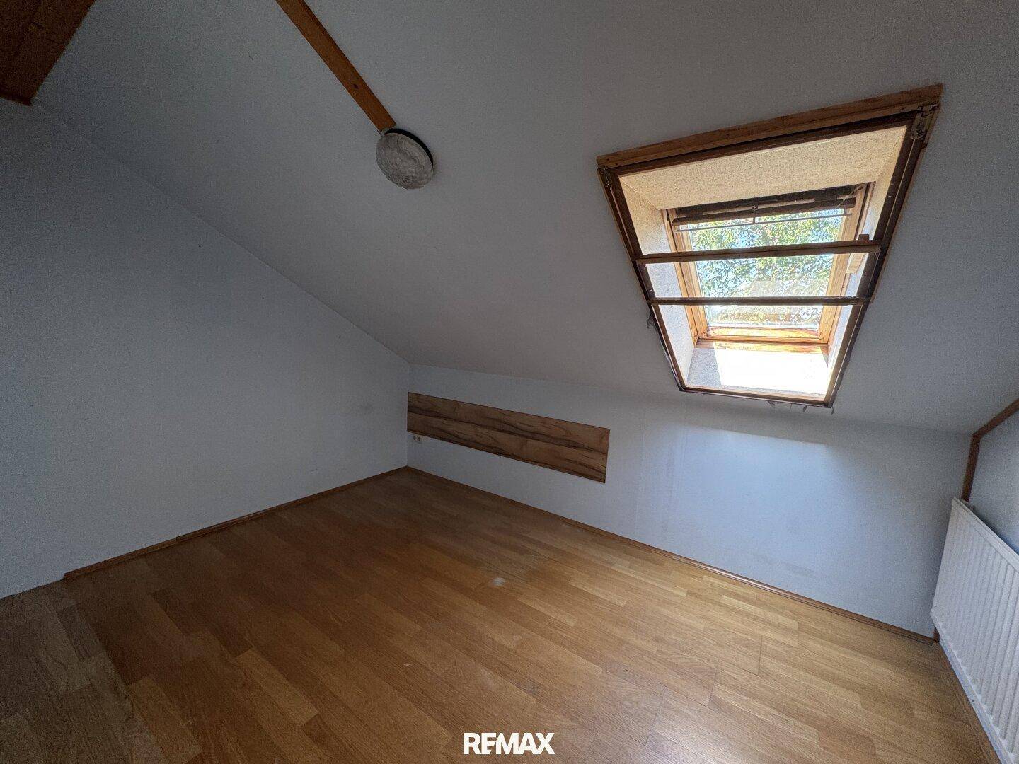 Helles Dachzimmer mit Holzboden, Dachfenster und schrägen Wänden.