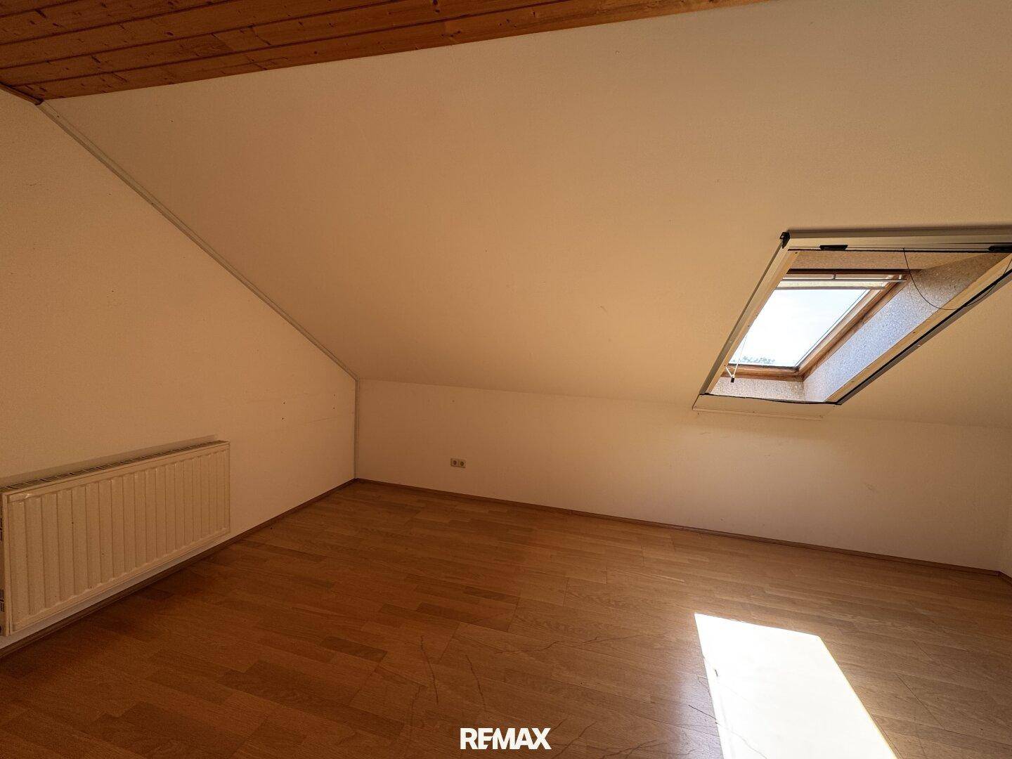 Helles Dachzimmer mit Holzdecke, Schrägdach und Dachfenster, ausgestattet mit Heizkörper und Holzfußboden.
