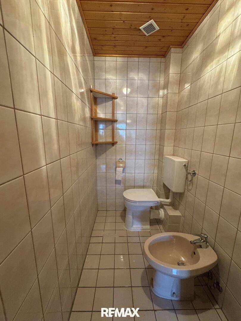 Kleines WC mit Fliesen an Wänden und Boden, ausgestattet mit Toilette, Bidet und Holzdecke.