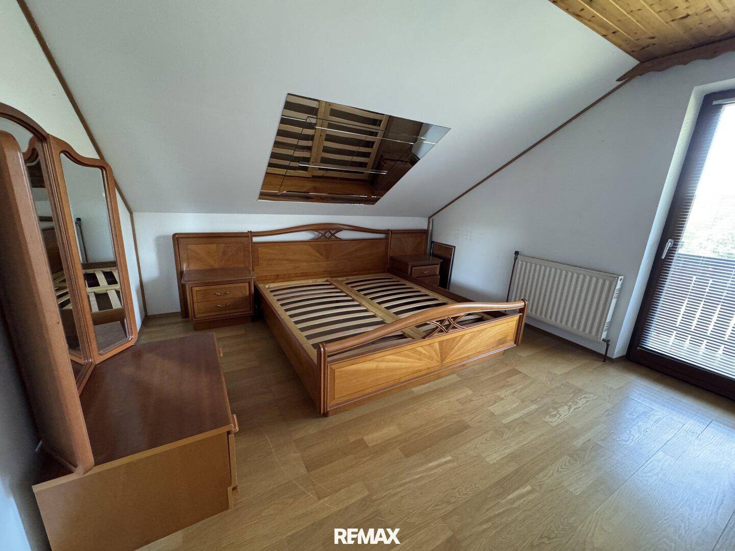 Helles Schlafzimmer im Dachgeschoss mit traditionellen Holzmöbeln, Holzdecke und großem Fenster.