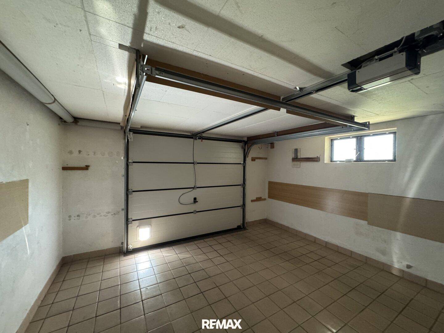 Geräumige Garage mit weißem Garagentor, Fliesenboden und einem kleinen Fenster für Tageslicht.