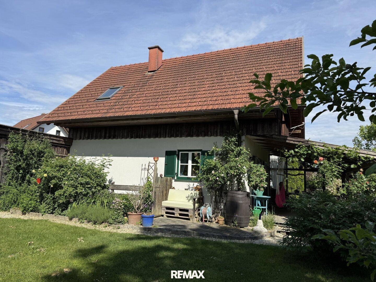 Seitlicher Blick auf das Haus mit Ziegeldach, weißer Fassade und einem gemütlichen Sitzbereich im Garten.