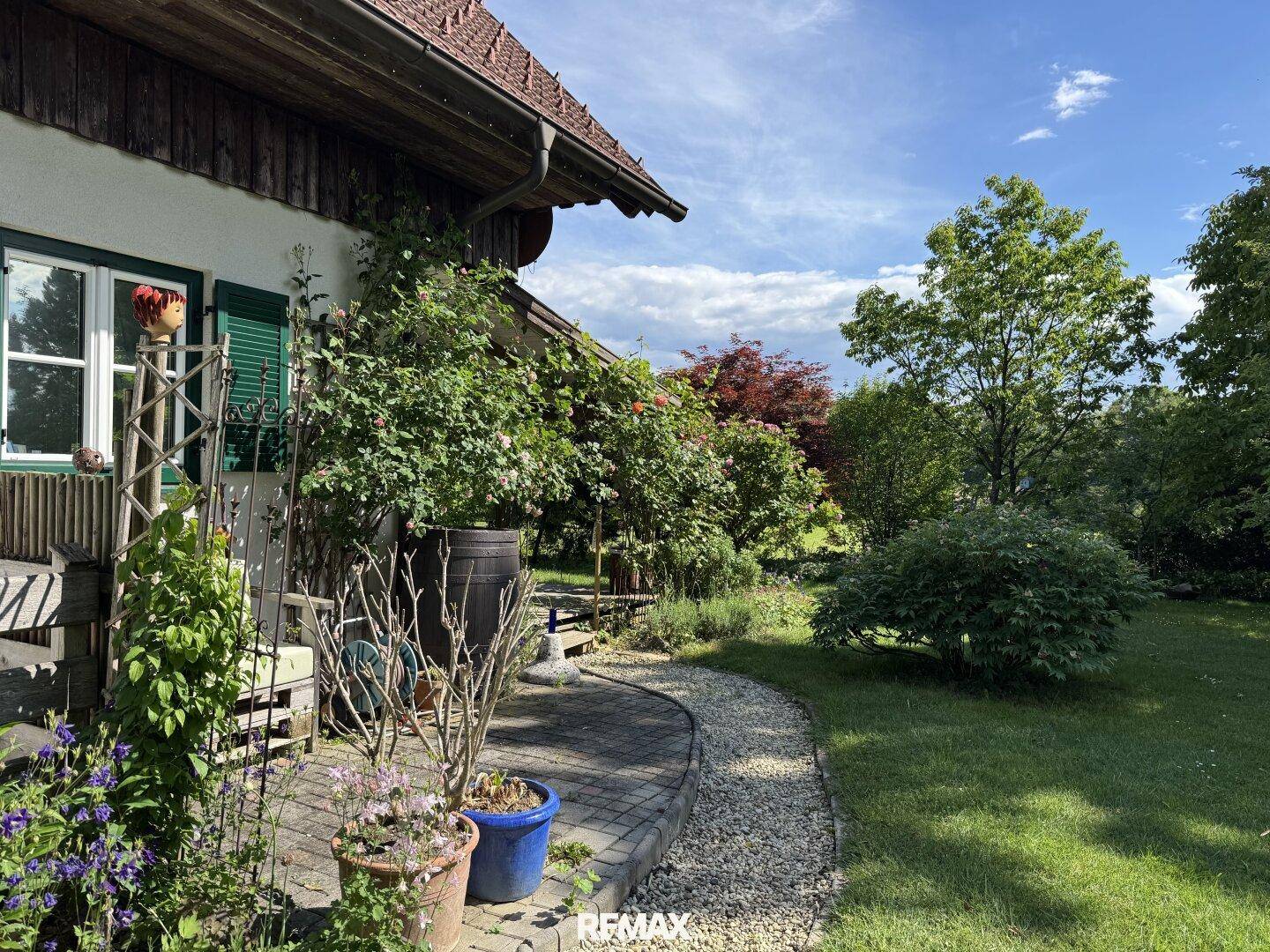Geschwungener Kiesweg im Garten, gesäumt von Blumen und Sträuchern, mit Blick auf die grüne Umgebung.