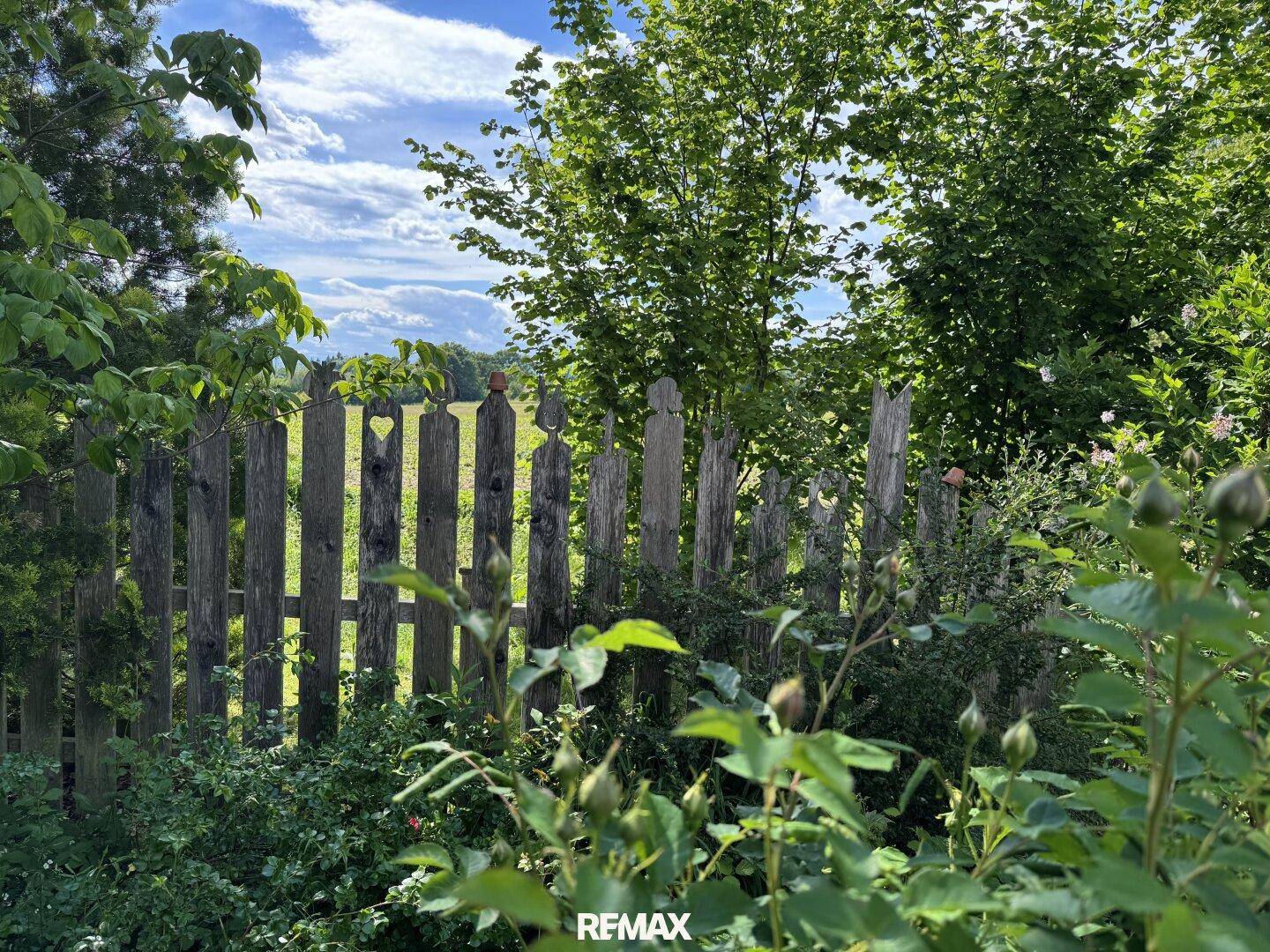 Rustikaler Holzzaun im Garten mit Blick auf weite Felder und grüne Landschaft.