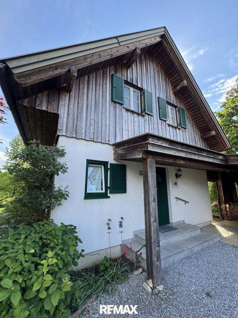 Eingangsbereich des Hauses mit weißer Fassade, grüner Tür und Holzverkleidung im Giebelbereich.