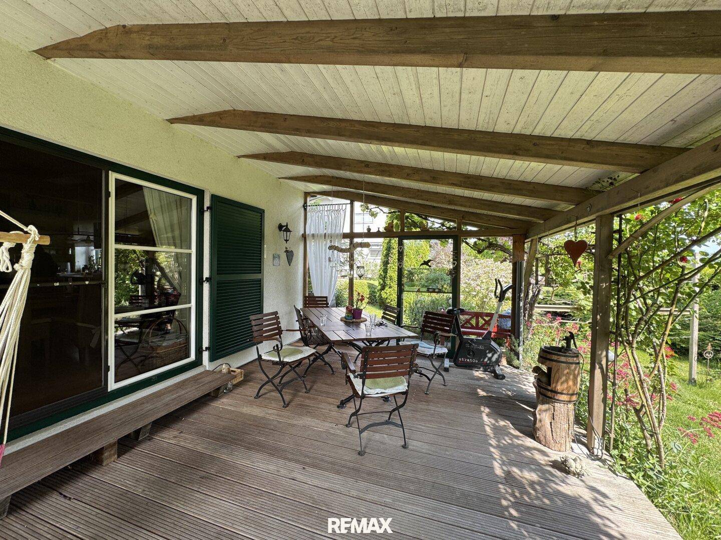 Geräumige überdachte Holzterrasse mit Esstisch und Stühlen, ideal für Mahlzeiten im Freien.