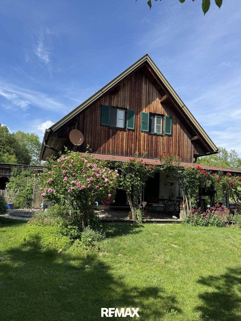 Idyllisches Holzhaus mit üppigem Rosengarten und sonniger Rasenfläche unter blauem Himmel.