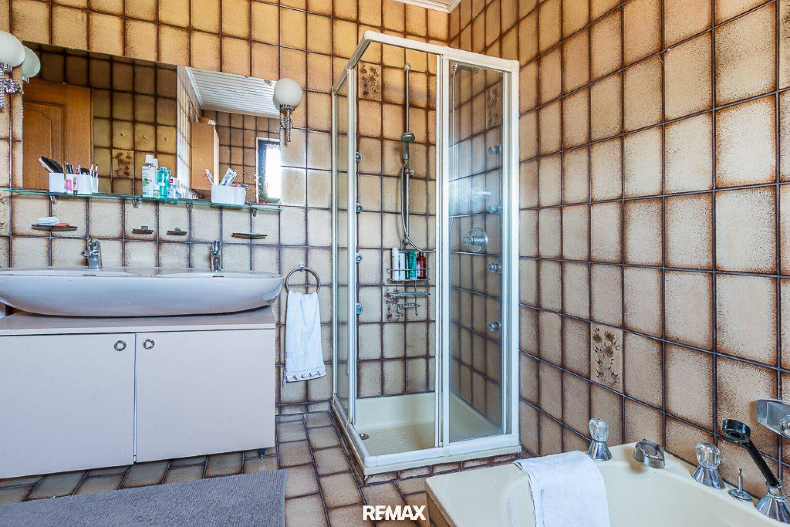 Badezimmer mit braunen Fliesen, Dusche und Badewanne, im Stil der 80er Jahre.