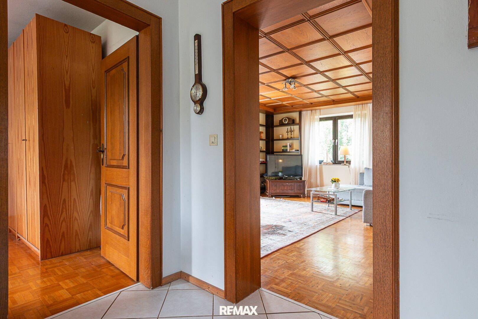 Flur mit Fliesenboden und Blick in ein Wohnzimmer mit Holzdecke und Parkett.