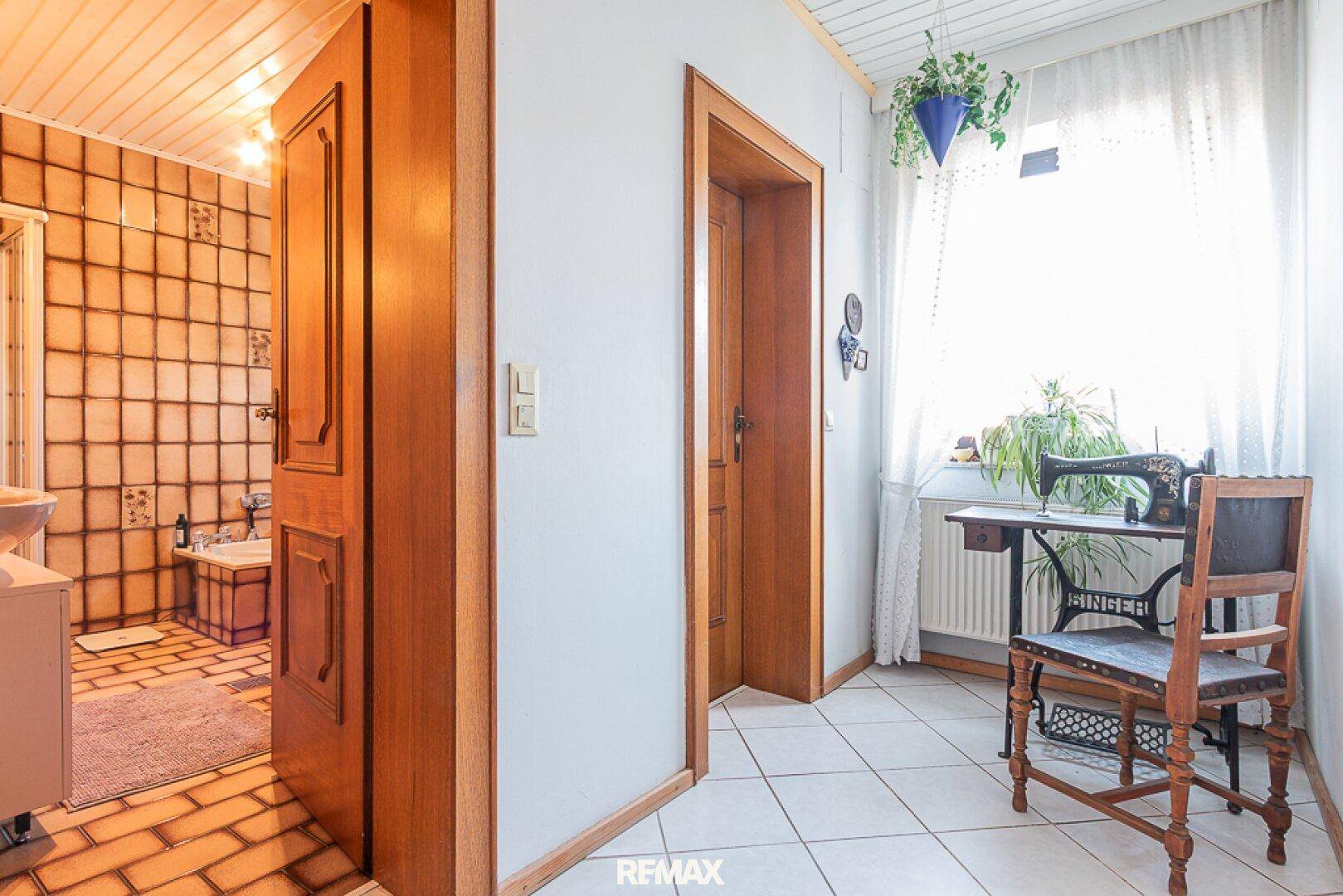 Flur mit Fliesenboden, Holztüren und Blick in ein Badezimmer und einen weiteren Raum.