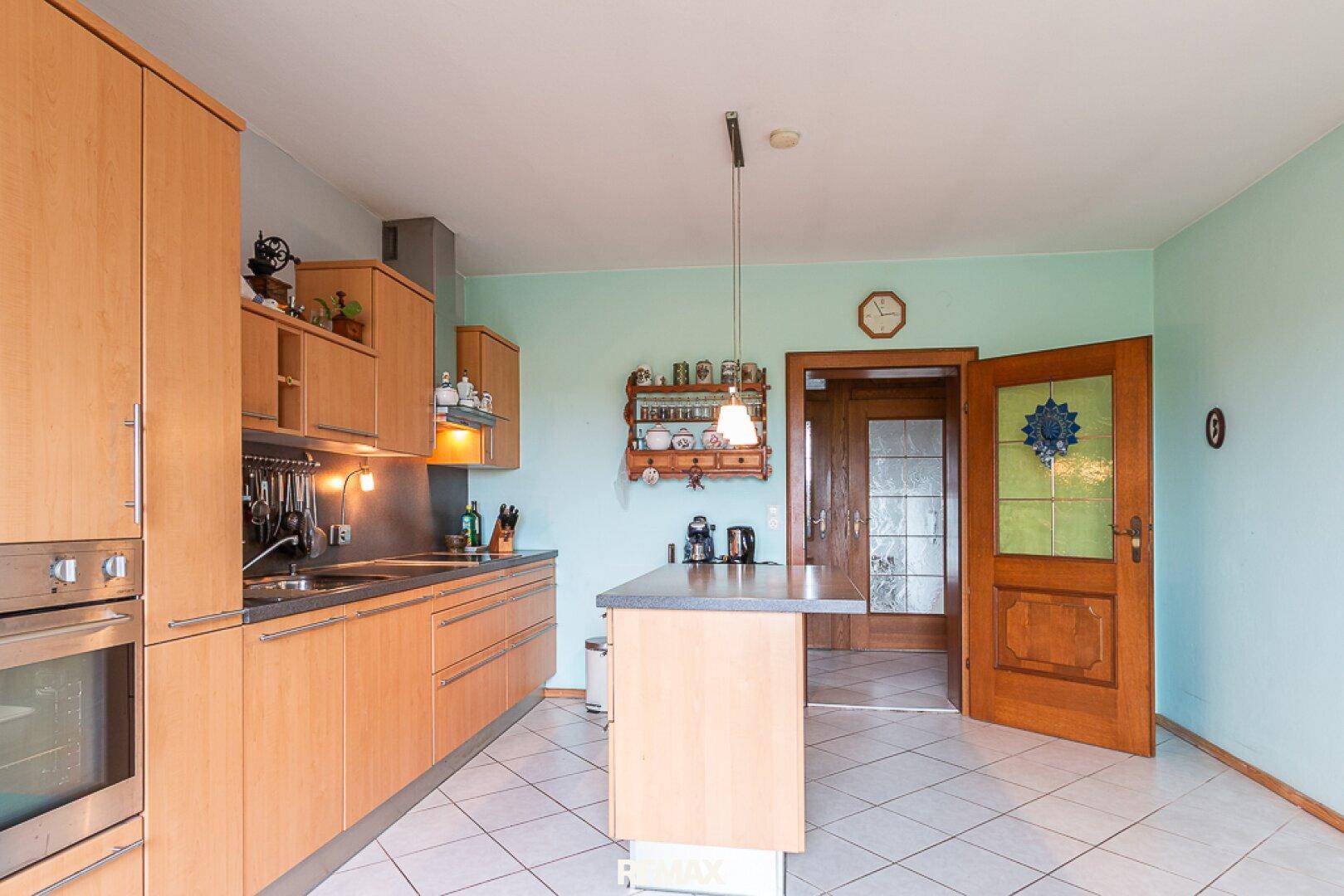 Küche mit Holzschränken, Kücheninsel und Blick auf eine Holztür mit Glaseinsatz.