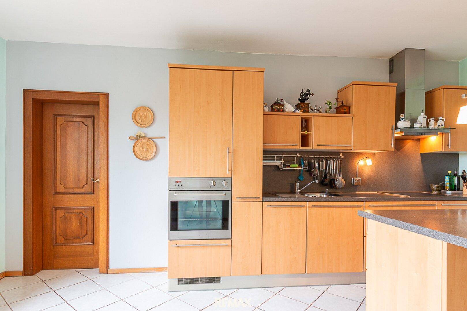 Einbauküche mit hellen Holzfronten, integriertem Backofen und Fliesenboden.