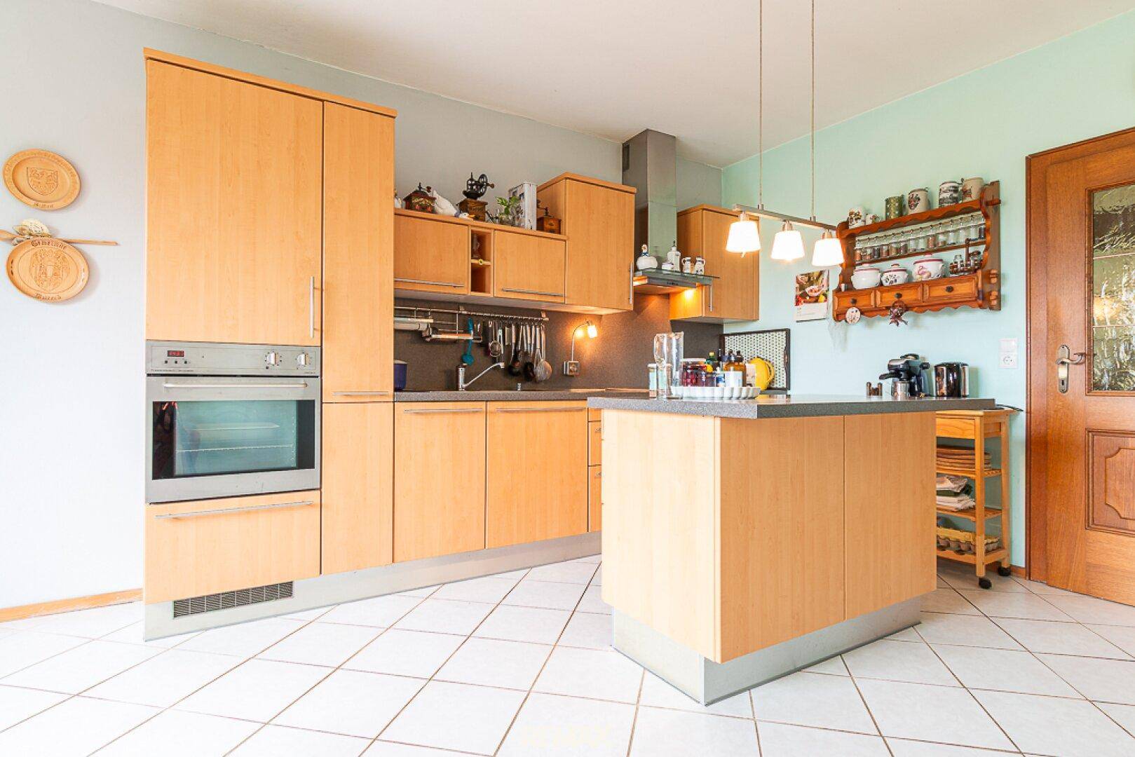 Helle Einbauküche mit Holzschränken, Kücheninsel und modernen Pendelleuchten.