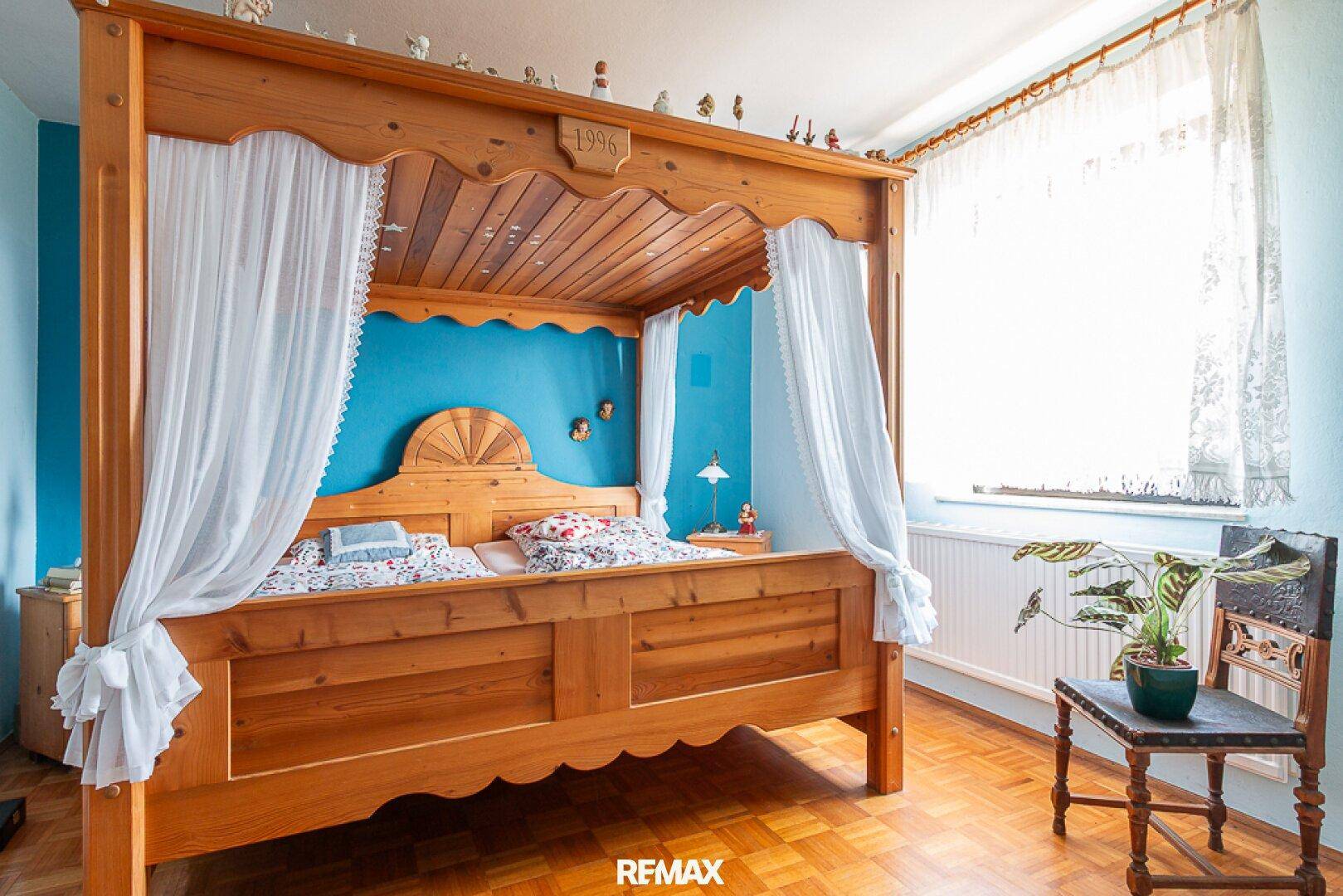 Gemütliches Schlafzimmer mit Himmelbett aus Holz, blauer Wand und Parkettboden.