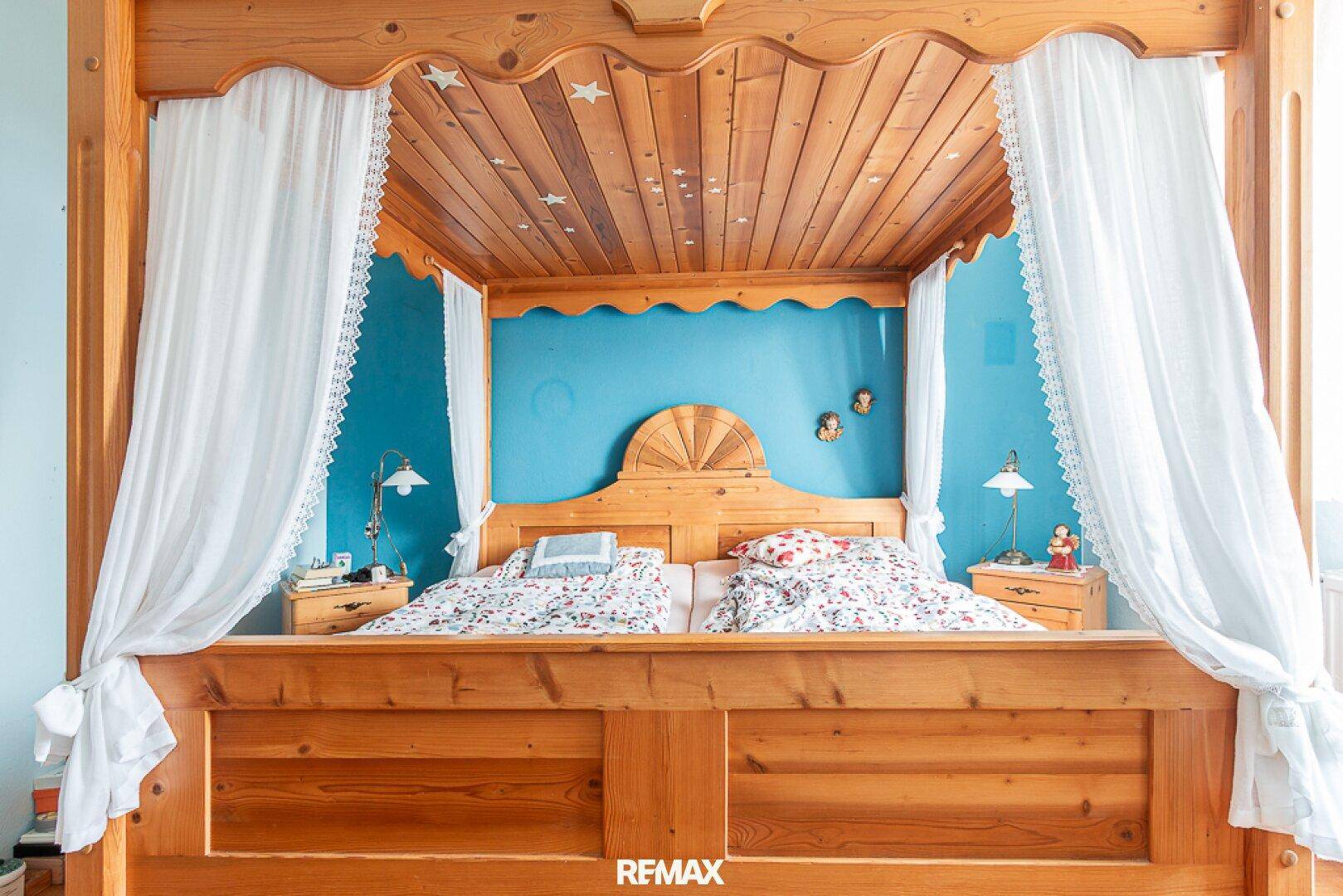 Nahaufnahme des Holzhimmelbettes mit blauer Wand und Nachttischen im Schlafzimmer.
