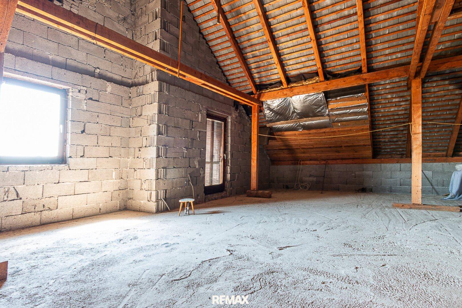 Unausgebauter Dachboden mit sichtbaren Holzbalken und Ziegelwänden, bereit für den Ausbau.