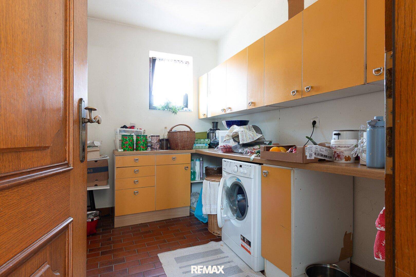 Praktischer Hauswirtschaftsraum mit Waschmaschine, orangefarbenen Schränken und Fliesenboden.
