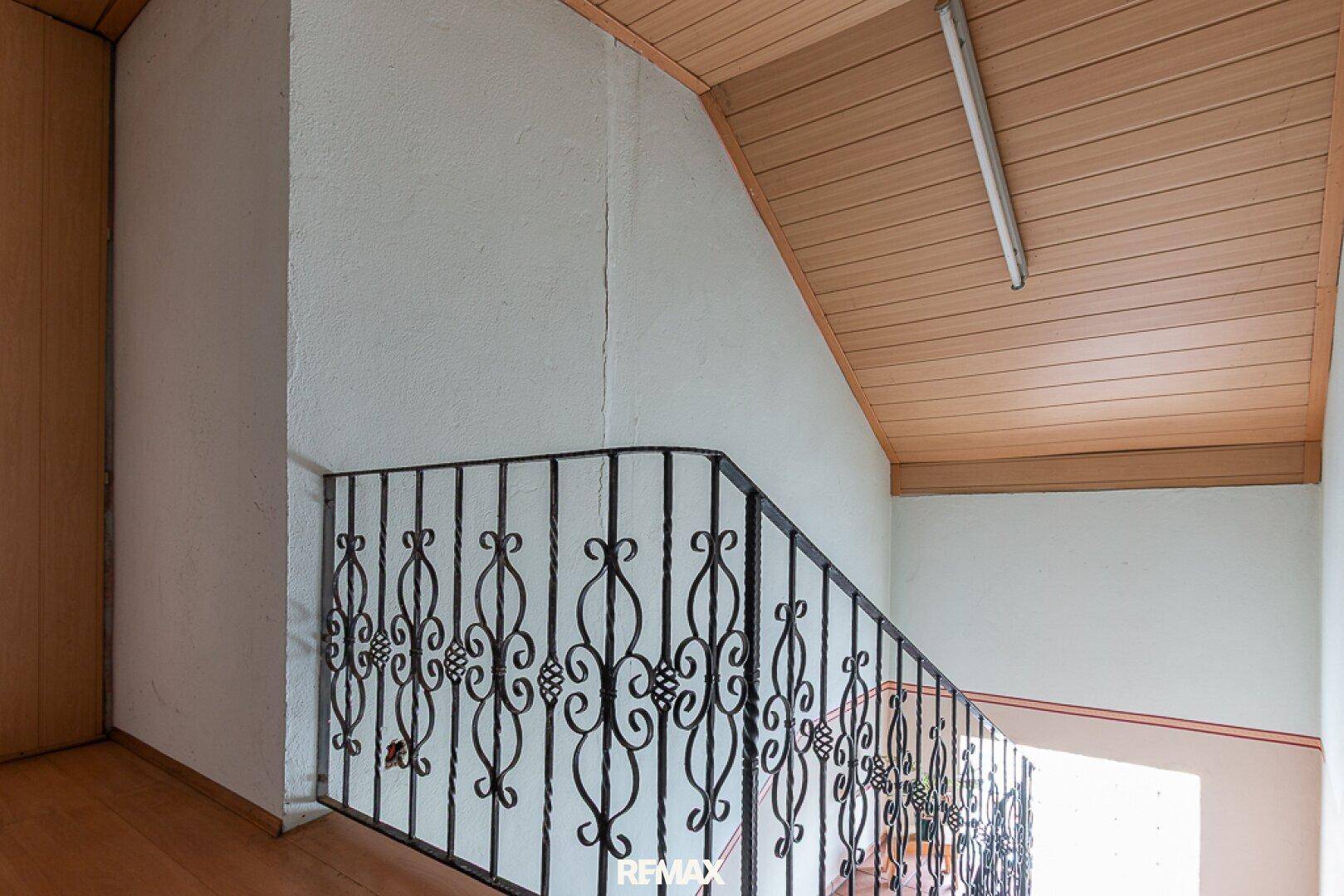 Treppenhaus mit schmiedeeisernem Geländer und Holzverkleidung an der Decke.