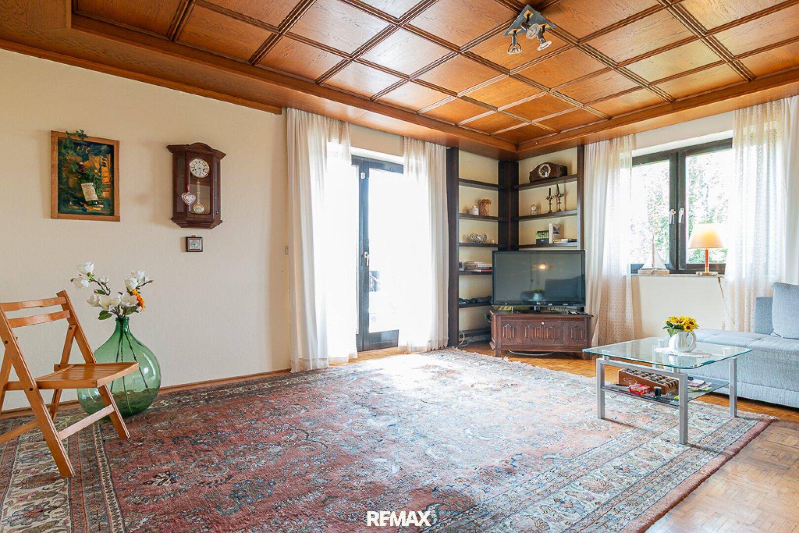 Helles Wohnzimmer mit Holzkassettendecke, beigem Sofa und traditionellem Teppich.