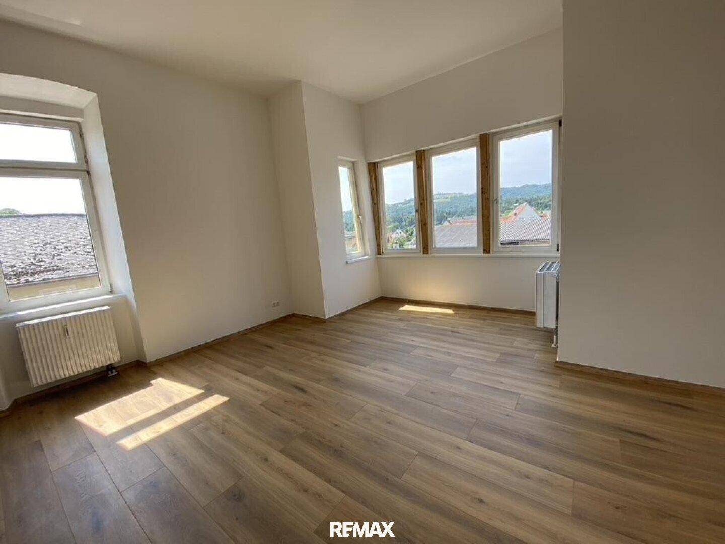 Helles Zimmer mit Laminatboden und mehreren Fenstern, die einen weiten Ausblick bieten.