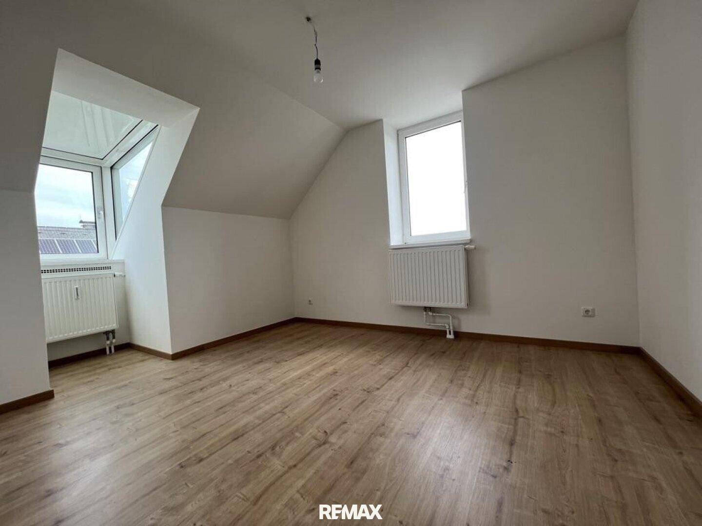 Dachgeschosszimmer mit schrägen Wänden, Laminatboden und einem Dachfenster.