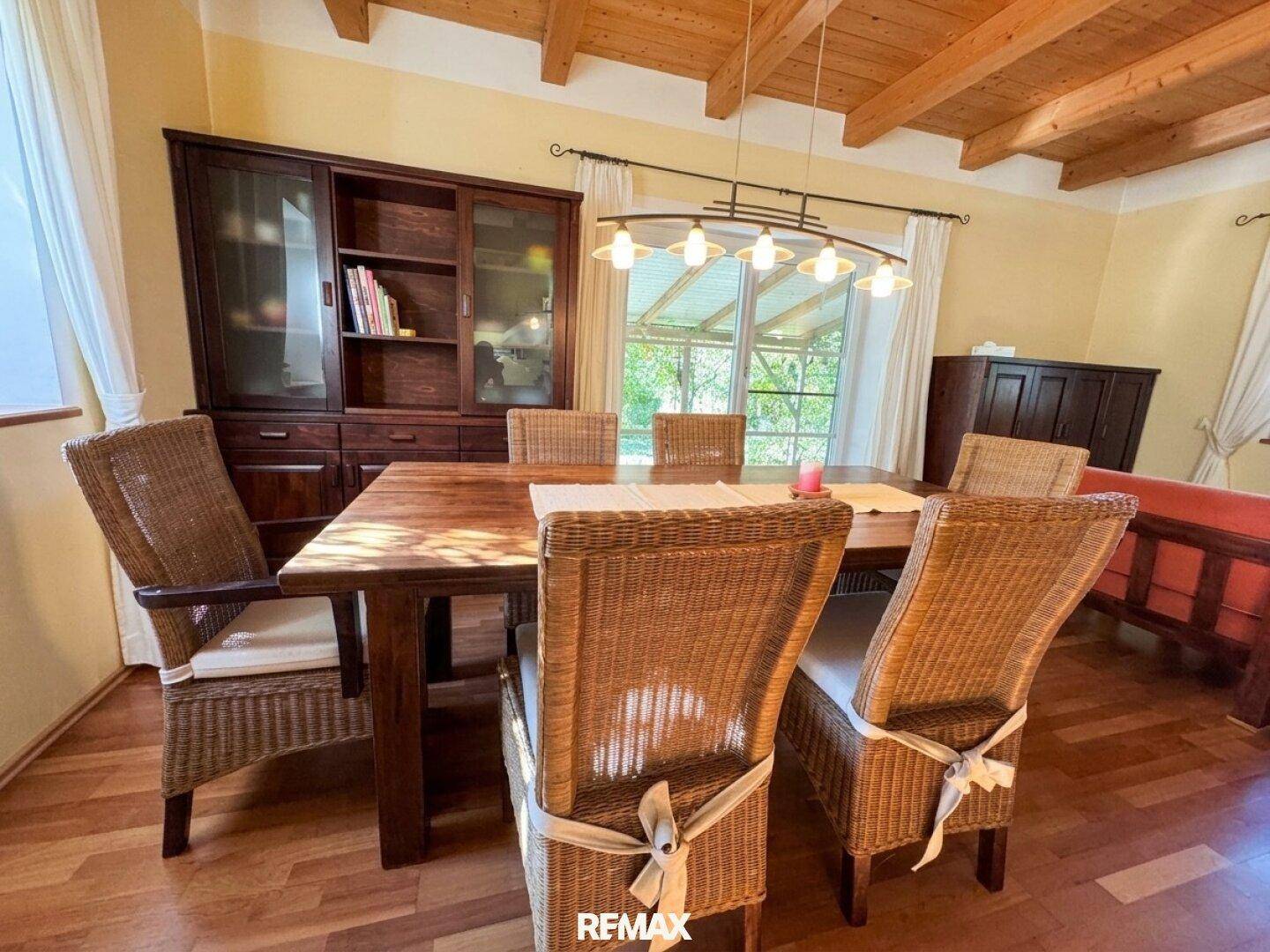 Gemütlicher Essbereich mit großem Holztisch, Korbstühlen und Blick in den Garten.